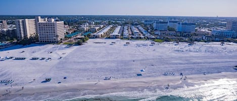 Una playa con filas de sillas y sombrillas, cielo despejado y edificios al fondo.