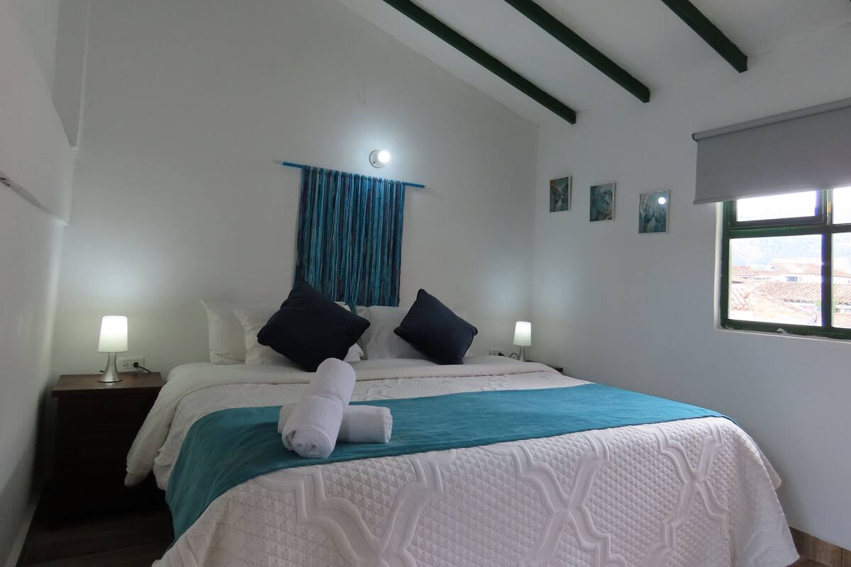 A bedroom with a bed, two bedside tables, a window, and a curtain.