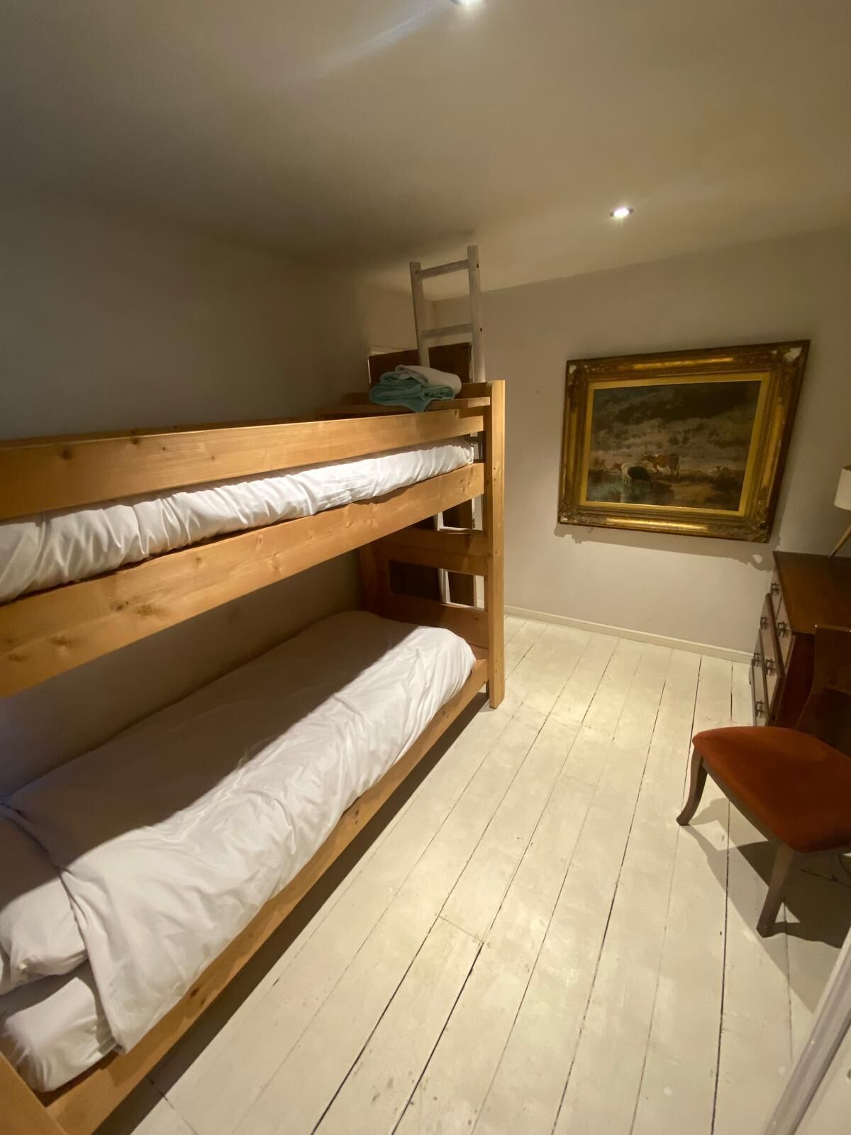 A bunk bed room with a ladder, a painting on the wall, and a chair.