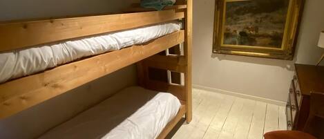 A bunk bed room with a ladder, a painting on the wall, and a chair.