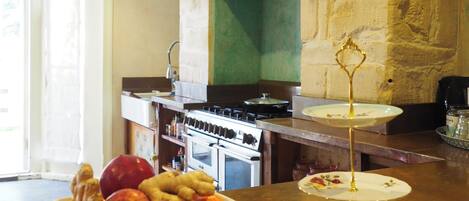 A kitchen with a stone wall, a bowl of fruit, a wine glass, and a stove.