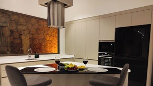A modern kitchen with a central island, bar stools, a stone backsplash, and a built-in oven. - Villa Sun 10 - PLANET LUXURY VILLAS (Kas)