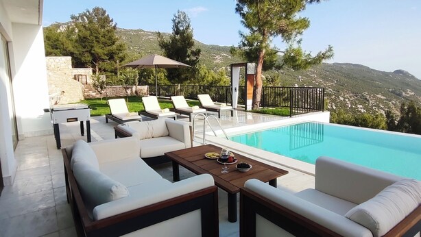 A poolside area with lounge chairs and a table, overlooking a pool and a mountainous landscape. - Villa Sun 10 - PLANET LUXURY VILLAS (Kas)