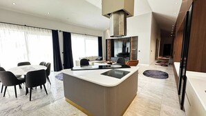 A modern kitchen with a central island, dining area with chairs, and a large window with curtains. - Villa Sun 10 - PLANET LUXURY VILLAS (Kas)