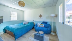 A modern bedroom with a bed, a blue sofa, a bedside table, and a large window. - Marée Basse - Studio proche plage de la potinière (Barneville-Carteret)