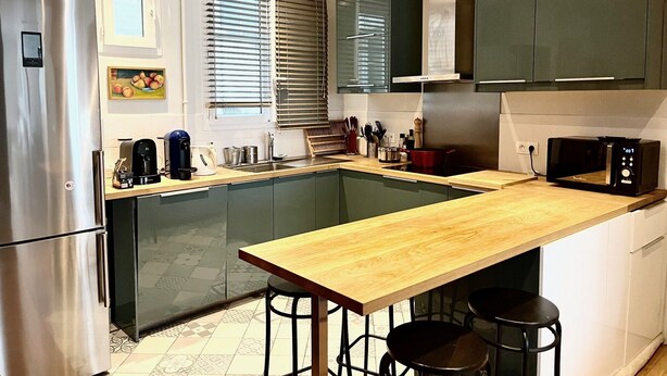 Une cuisine moderne dotée d’un îlot central, d’appareils électroménagers en acier inoxydable et de meubles de rangement aux couleurs sombres.