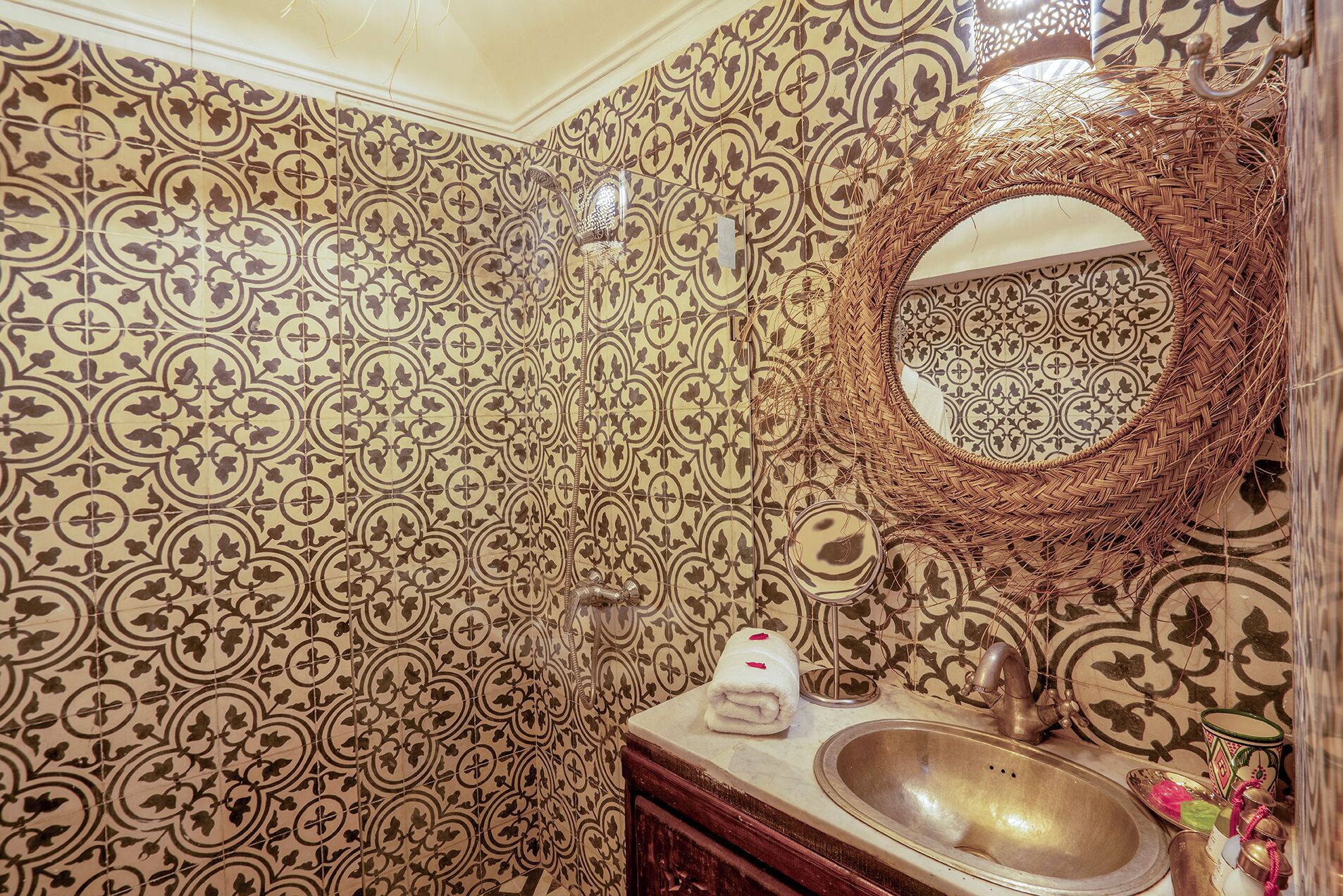 A bathroom with patterned tiles, a round mirror, a sink, and a towel.