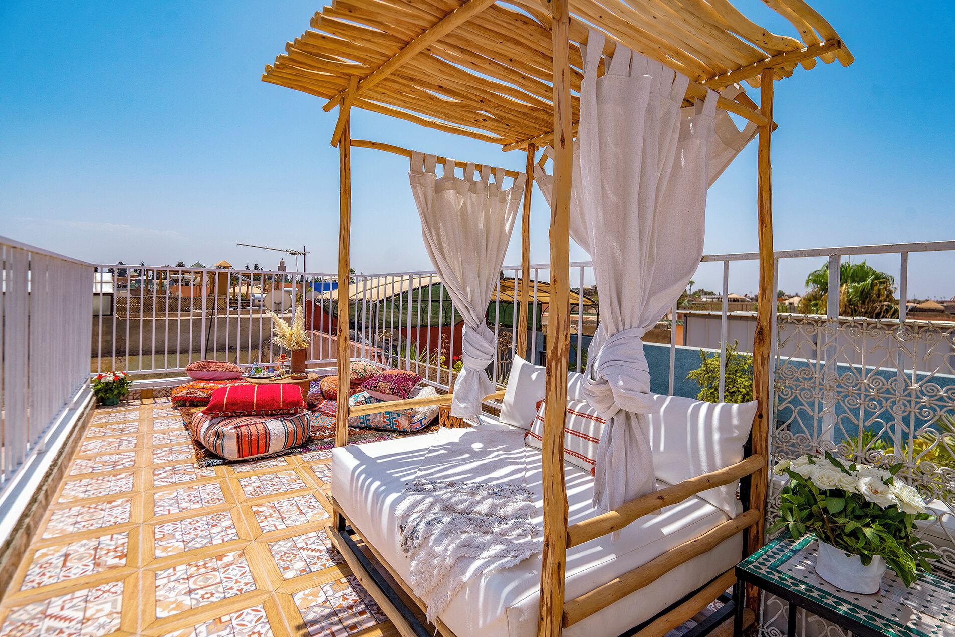 A rooftop terrace with a wooden canopy bed, patterned floor tiles, and a view of the surrounding area.