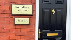Eine schwarze Tür mit einer Messingklopfer und einem goldenen Griff. Oberhalb der Tür befinden sich zwei Schilder: eines zeigt 'Roundtree & Berry APARTMENTS' und das andere die Adresse '33a & 33b NORTH ALBERT ST'.