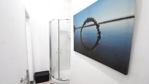 Eine Glasdusche, eine schwarze Tür und ein an der Wand befestigtes Bild von ruhigem Wasser mit einer kreisförmigen Steinformation.
