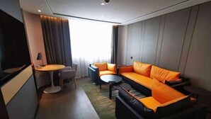 A modern hotel room with a sofa, a small table, a chair, and a television.