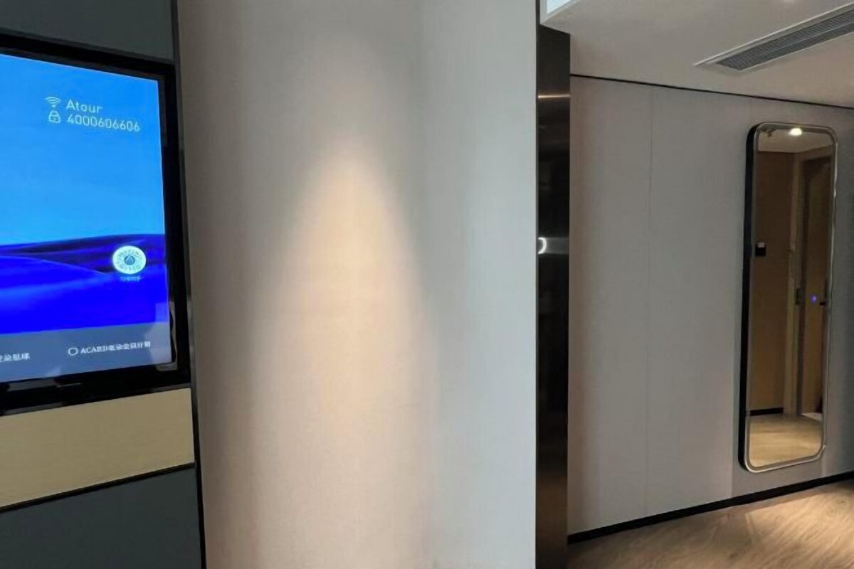 Ein modernes Hotelzimmer mit einem großen Bildschirm, der Zimmerdetails anzeigt, einem Spiegel und einer Tür.