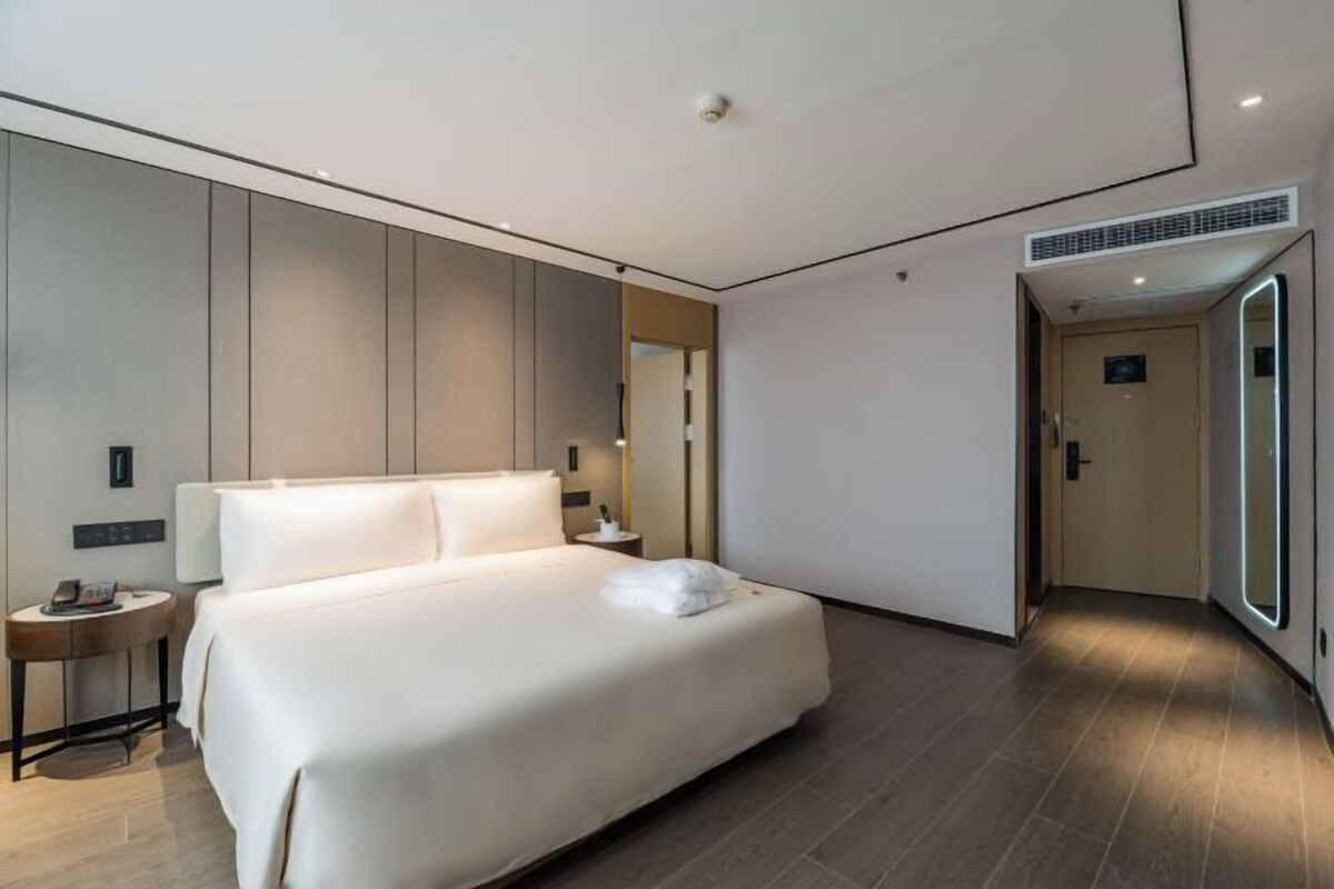Ein modernes Hotelzimmer mit einem großen Bett, Nachttischen, einem Spiegel und einer Tür zu einem weiteren Raum.