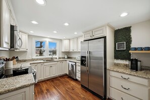 A modern kitchen with white cabinets, granite countertops, a stainless steel refrigerator, and a window providing natural light. - Historic Downtown Home with Fire Pit (Leesburg)