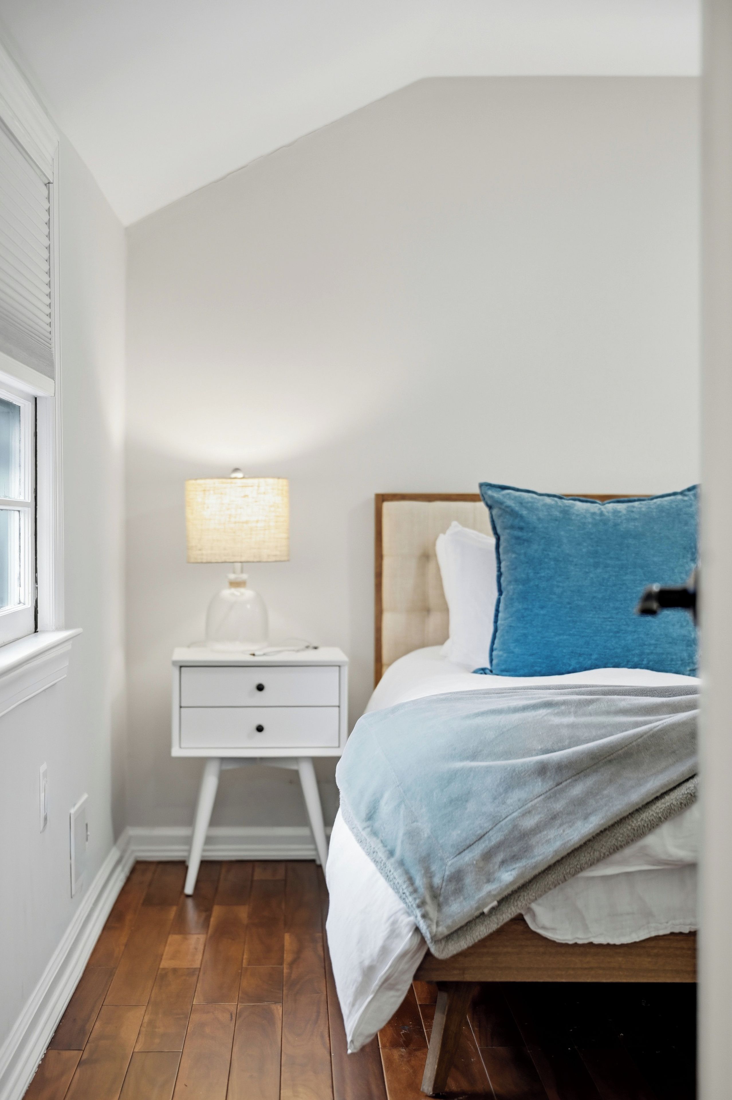 Een slaapkamer met een bed, nachtkastje, lamp en raam.