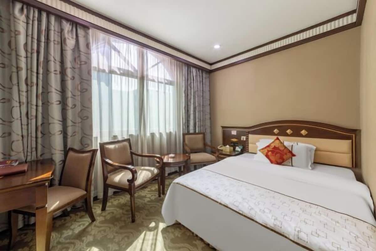 Een hotelkamer met een bed, twee stoelen, een klein tafeltje en een bureau.