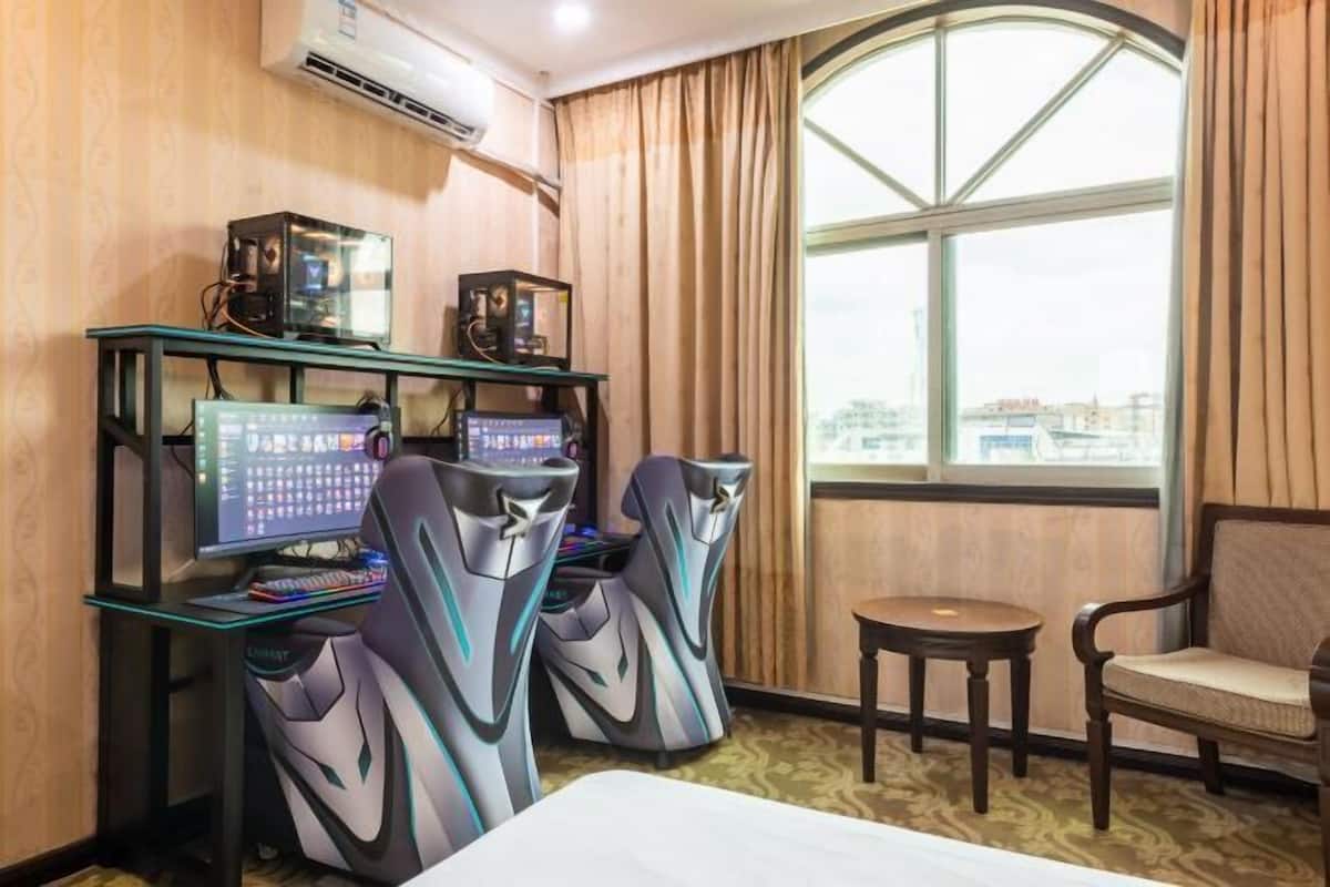 Een hotelkamer met een bureau, twee gaming stoelen, een computer en een bijzettafeltje.