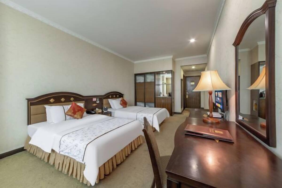 Een hotelkamer met twee bedden, een houten bureau, een spiegel en een lamp.