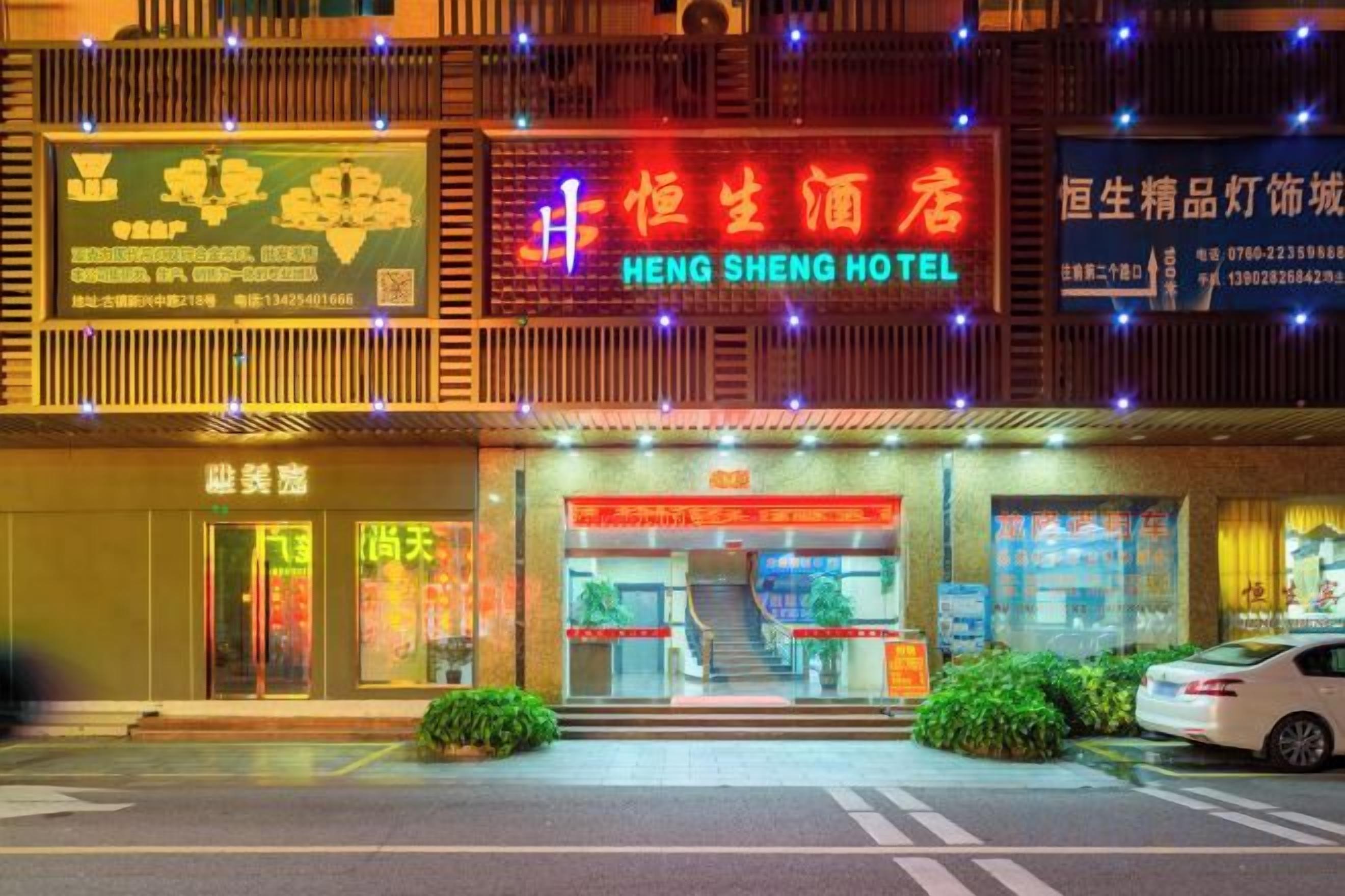 A hotel with a red sign, a staircase leading to the entrance, and a car parked outside.