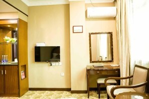 Une chambre d’hôtel équipée d’un téléviseur à écran plat fixé au mur, d’un bureau avec une chaise, d’un miroir et d’une fenêtre avec des rideaux.