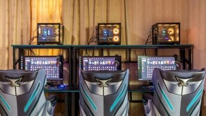 Een gaming-opstelling met drie monitoren, een glazen bureau en twee luxe gaming-stoelen.