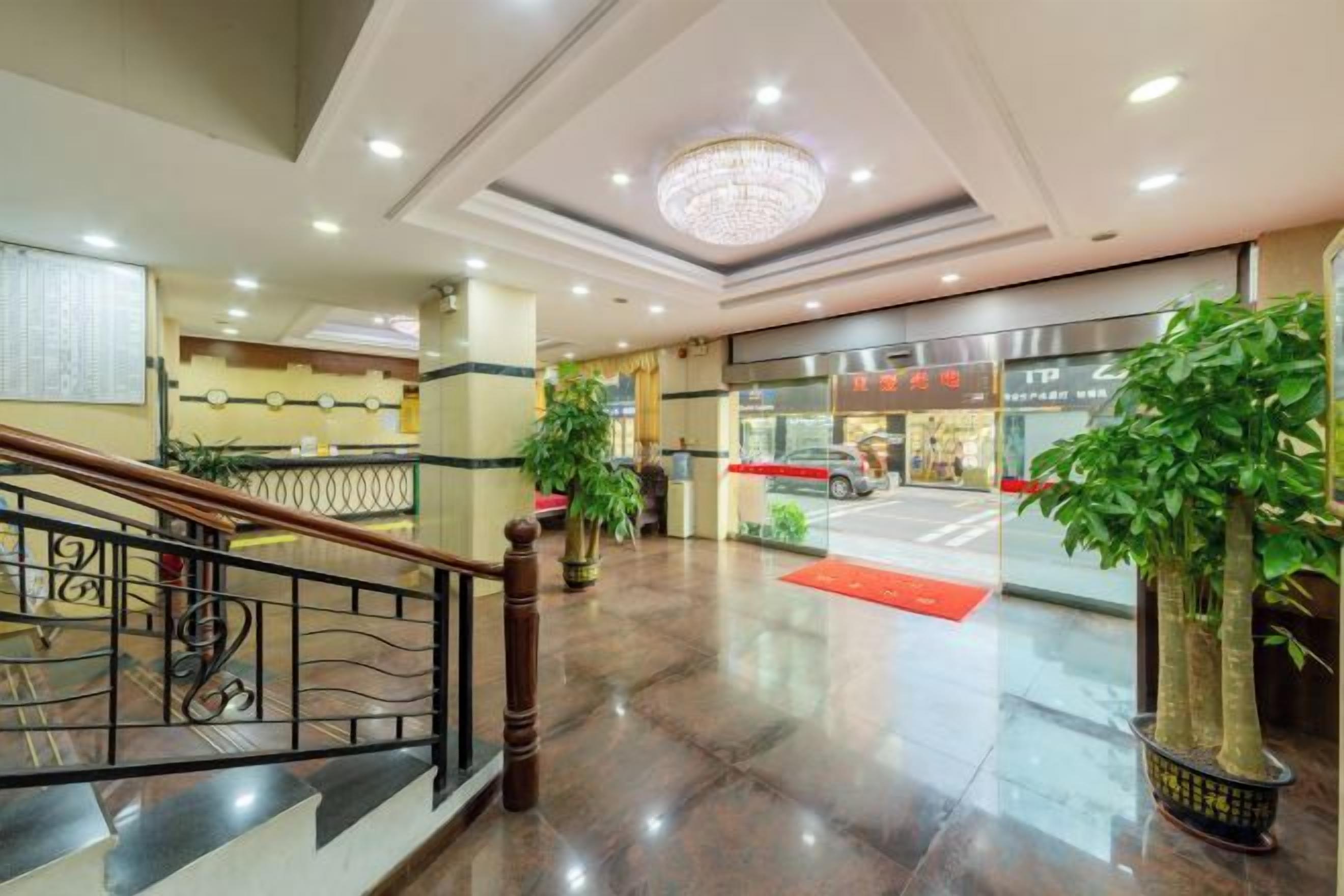 A hotel lobby with a staircase, a reception desk, and a large chandelier.