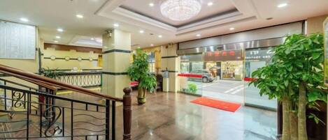 A hotel lobby with a staircase, a reception desk, and a large chandelier.