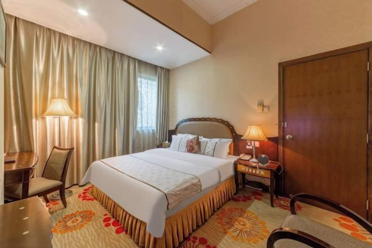 Een hotelkamer met een bed, nachtkastjes, een bureau, een stoel, een kledingkast en een raam met gordijnen.