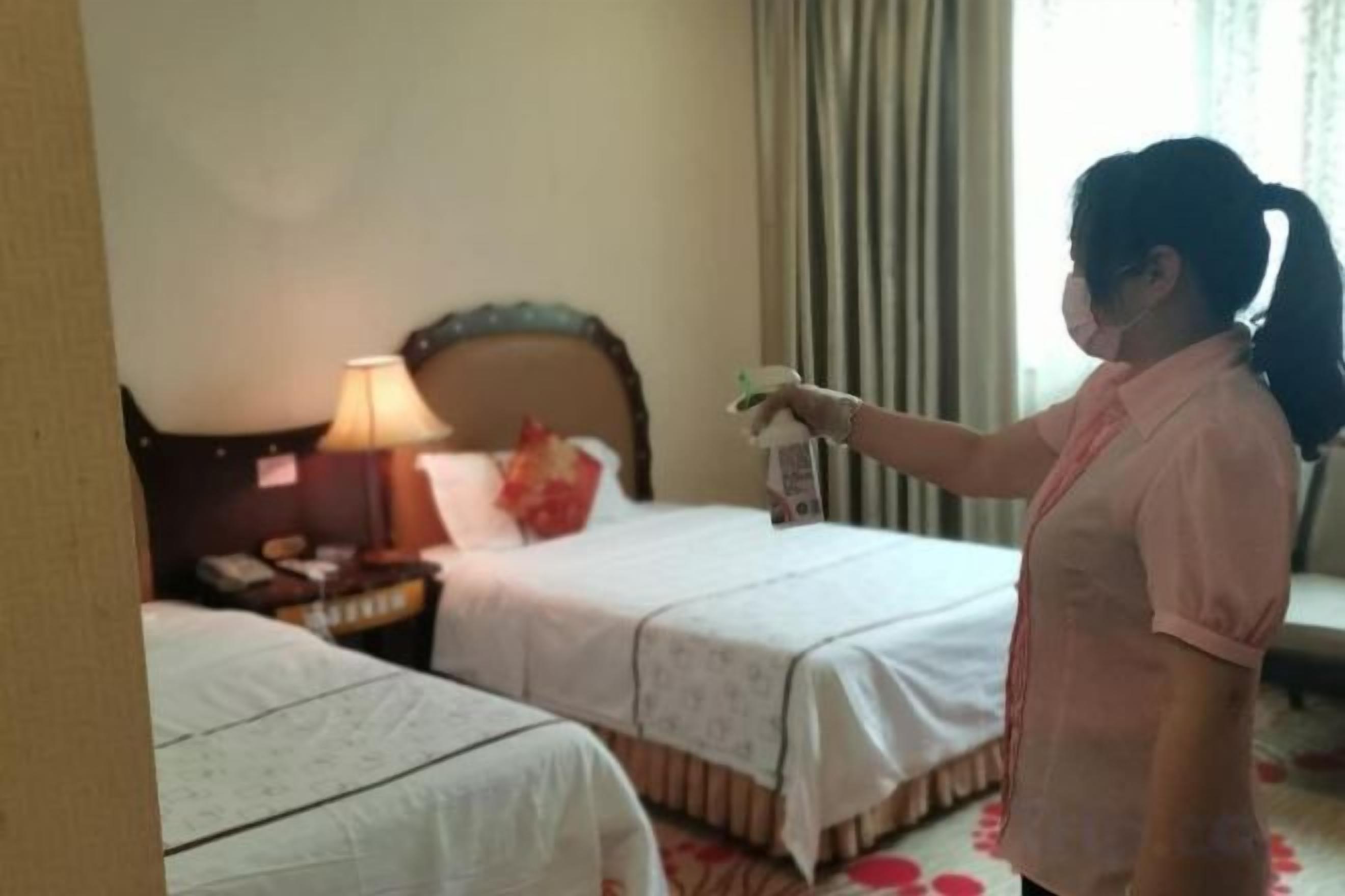 A hotel room with two beds, a nightstand with a lamp, and a window with curtains.