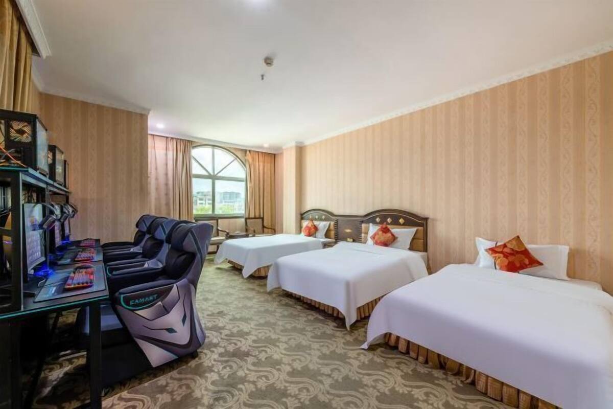 Een hotelkamer met drie bedden, een bureau met een computer en een massagestoel.