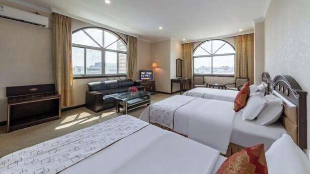 Een hotelkamer met twee bedden, een bank, een televisie en grote ramen.