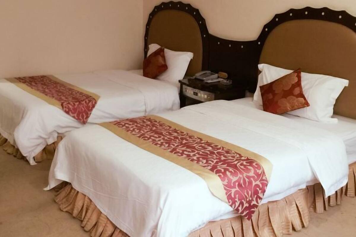 Een hotelkamer met twee bedden, elk met een witte spreidek en een rode en gouden decoratierand.