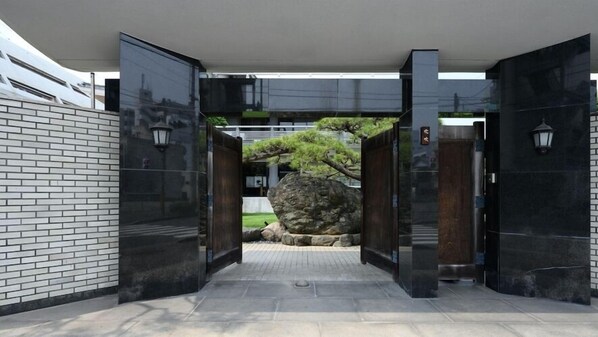 Una entrada moderna con puertas negras, un muro de ladrillo y un detalle de piedra.