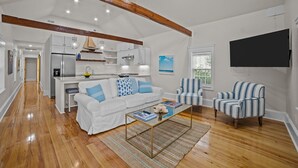 A spacious living room with a white sofa, striped armchairs, a coffee table, and a kitchen in the background. - The Cottage in Little Washington (Washington)