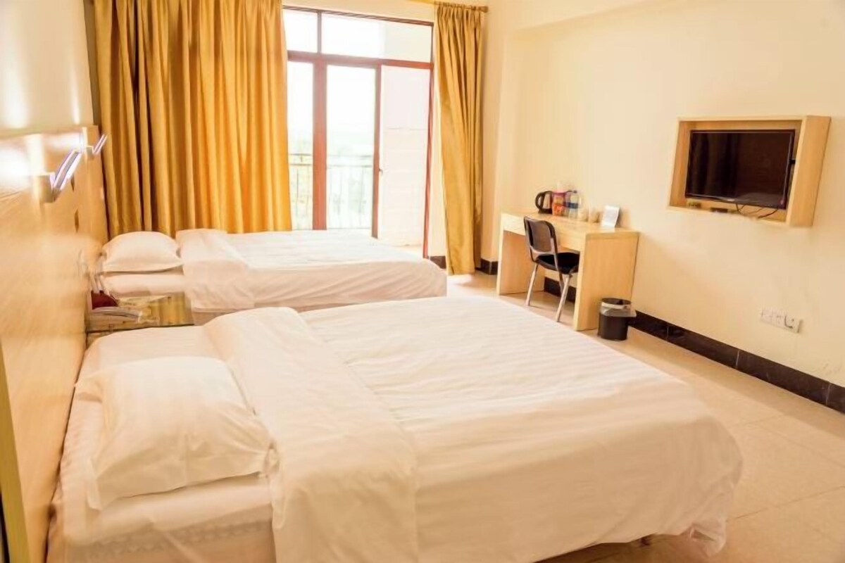 Ein Hotelzimmer mit zwei Betten, einem Schreibtisch, einem Stuhl, einem Fernseher und einem Fenster mit Vorhängen.