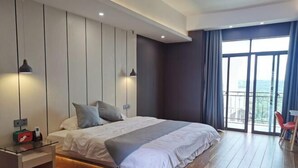 Quarto moderno com uma cama grande, uma mesa de cabeceira de vidro e vista para o exterior através de uma janela ampla.