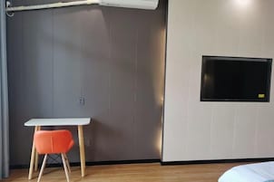 Una habitación moderna con un televisor de pantalla plana en la pared, una mesita pequeña con una silla naranja y suelo de madera.