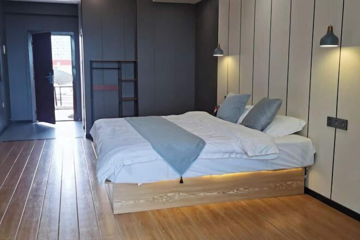 Un dormitorio moderno con suelo de madera, cama con ropa blanca y dos luces fijadas a la pared.