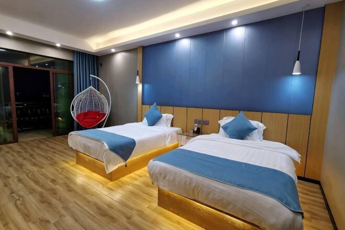 Habitación de hotel con dos camas, un sillón colgante y un ventanal grande.