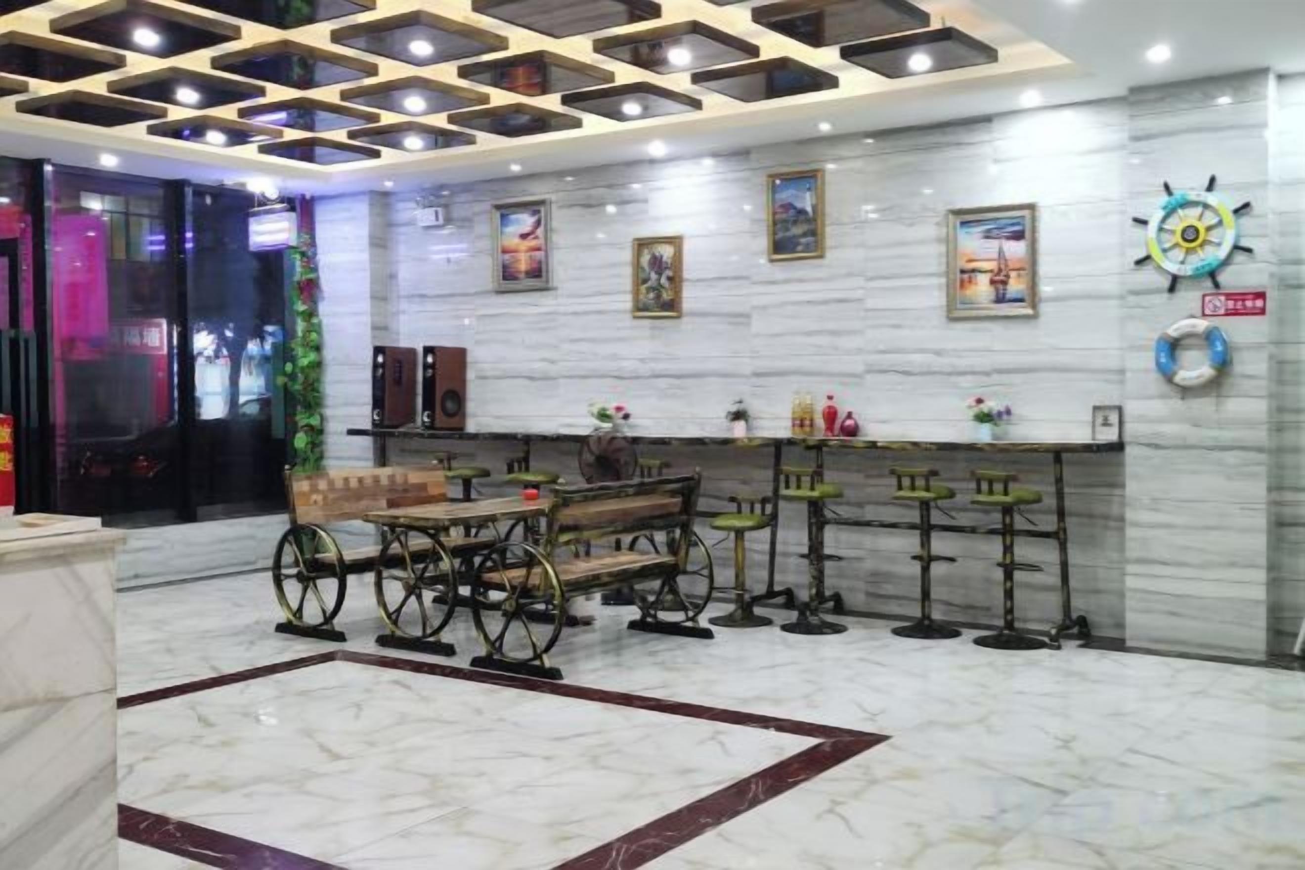 Un hall con piso de mármol, un banco de madera, una zona de bar con taburetes y una pared con cuadros enmarcados y un reloj.