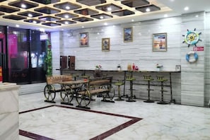 A lobby with a marble floor, a wooden bench, a bar area with stools, and a wall with framed pictures and a clock. - Shanshui Shiji Holiday Hotel (Wenchang)