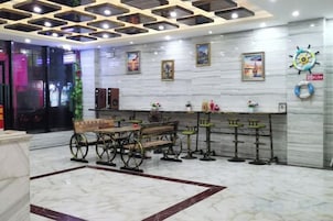 Un hall con piso de mármol, un banco de madera, una zona de bar con taburetes y una pared con cuadros enmarcados y un reloj.