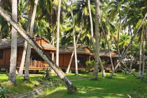 A bungalow-style accommodation with a thatched roof, surrounded by lush greenery and palm trees. - Shanshui Shiji Holiday Hotel (Wenchang)