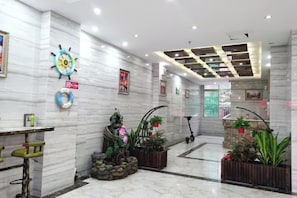 A hotel lobby with marble walls, a reception desk, potted plants, and a ceiling with recessed lighting. - Shanshui Shiji Holiday Hotel (Wenchang)