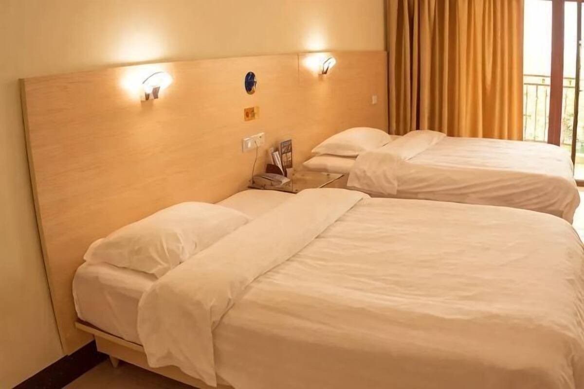Habitación de hotel con dos camas, cabecero de madera, lámparas de noche y una ventana con cortinas.