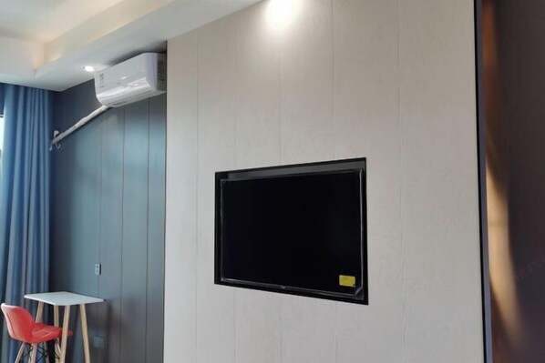 Ein Zimmer mit einem an der Wand befestigten Fernseher, einem kleinen Tisch und einem roten Stuhl.