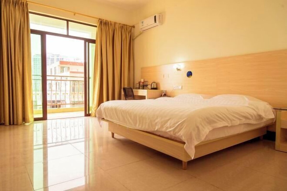 Ein Hotelzimmer mit Bett, Schreibtisch, Stuhl, einem Fenster mit Vorhängen und einer Klimaanlage.