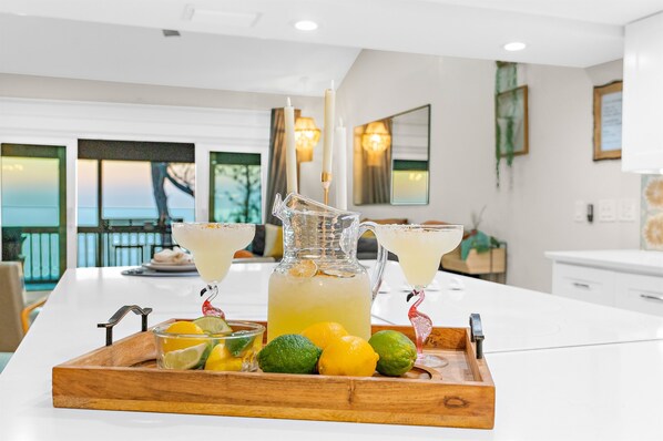 A kitchen with a white countertop, a pitcher of lemonade, lime wedges, and two glasses of lemonade on a wooden tray.