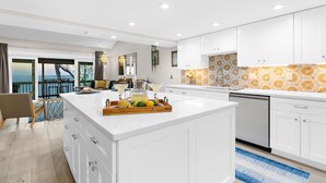 Une cuisine moderne avec des meubles blancs, un îlot central sur lequel est posé un plateau de citrons, et un pare-feu décoré de motifs.
