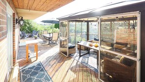 A covered patio area with outdoor furniture, a glass enclosure, and a view of the surrounding garden. - City Escape-Cottage by the Lake (Brampton)